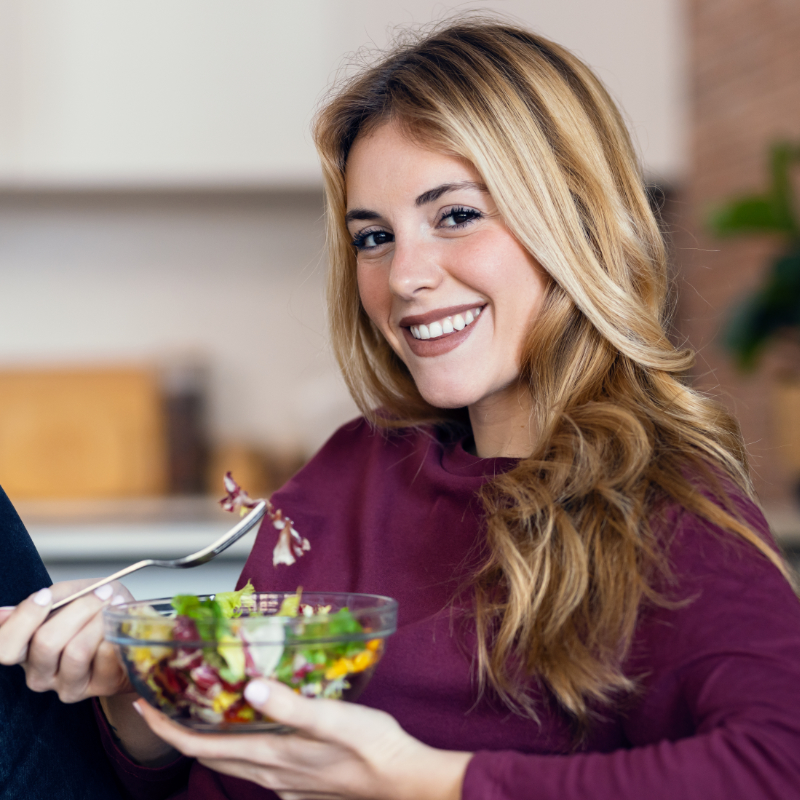 Beautiful smiling woman eating healthy salad while sitting in the kitchen at home.